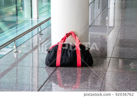 Suspicious black and red bag left unattended in an empty hall. Dangerous ownerless derelict luggage. 92036762