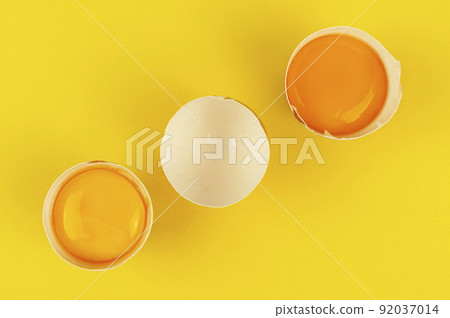Raw egg yolks in the halves of cracked brown eggshells on yellow background Raw egg yolks in the halves of cracked brown eggshells on yellow background 92037014