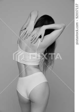 Portrait of young girl with slim tender figure posing in white underwear. Black and white photography aesthetics 92037137