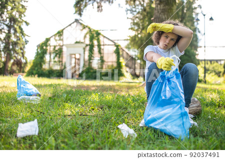 Cute young volunteer looking tired after gathering garbage Cute young volunteer looking tired after gathering garbage 92037491