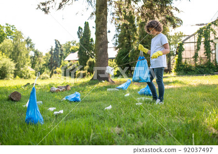 Cute young volunteer cleaning the park from plastic garbage Cute young volunteer cleaning the park from plastic garbage 92037497