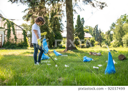 Cute young volunteer cleaning the park from plastic garbage Cute young volunteer cleaning the park from plastic garbage 92037499