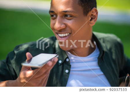 Guy recording voice message on smartphone looking away 92037533