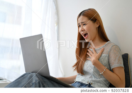 Amazed and excited young Asian woman receiving unexpected news through her laptop computer. 92037828