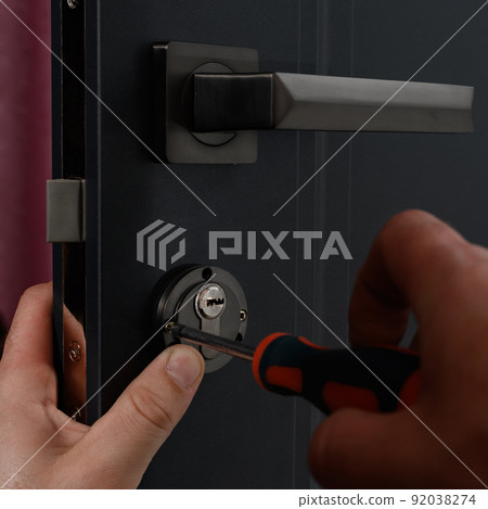 Installation of a door lock, a carpenter installs a door lock in a door, work close-up. 92038274