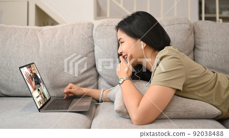 Young woman in casual wears lying on couch and communication through video chat 92038488