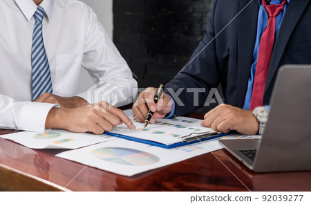 Two business leaders talk about charts, financial graphs showing results are analyzing and calculating planning strategies, business success building processes Two business leaders talk about charts, financial graphs showing results are analyzing and calculating planning strategies, business success building processes 92039277