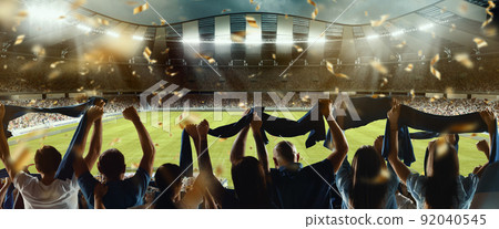 Back view of football, soccer fans cheering their team with colorful scarfs at crowded stadium at evening time. Concept of sport, support, competition. Out of focus effect 92040545