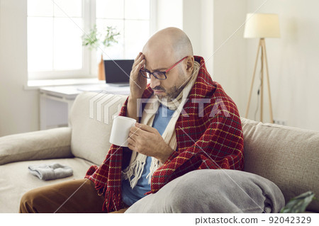 Unhappy joyless sick man at home treats flu and colds with medicinal drink with unpleasant taste. 92042329