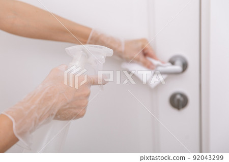 Cleaning door handles with wet wipe and white gloves. Sanitize surfaces prevention in hospital and public spaces against corona virus. Woman hand using towel for cleaning home room door link. 92043299