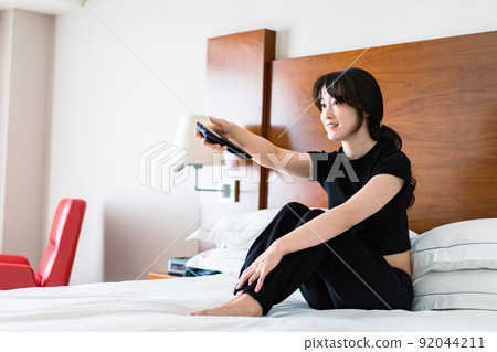 一位年輕女子用遙控器操作電視 一位年輕女子用遙控器操作電視 92044211