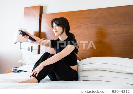 一位年輕女子用遙控器操作電視 一位年輕女子用遙控器操作電視 92044212