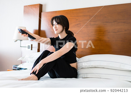 一位年輕女子用遙控器操作電視 一位年輕女子用遙控器操作電視 92044213