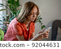 Young female using smartphone at home checking email, writing message in social network, searching information.  92044631