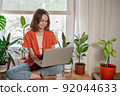 Young female using laptop at home checking email, writing message in social network, searching information. Cozy workplace, remote work learning concept. 92044633