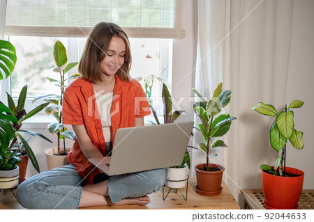 Young female using laptop at home checking email, writing message in social network, searching information. Cozy workplace, remote work learning concept. 92044633