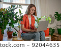 Young female using laptop at home checking email, writing message in social network, searching information. Cozy workplace, remote work learning concept. 92044635