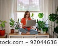 Young female using laptop at home checking email, writing message in social network, searching information. Cozy workplace, remote work learning concept. 92044636