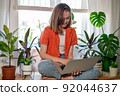 Young female using laptop at home checking email, writing message in social network, searching information. Cozy workplace, remote work learning concept. 92044637