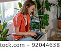 Young female using laptop at home checking email, writing message in social network, searching information. Cozy workplace, remote work learning concept. 92044638