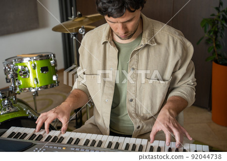 Young man plays synthesizer in equipped music studio Young man plays synthesizer in equipped music studio 92044738