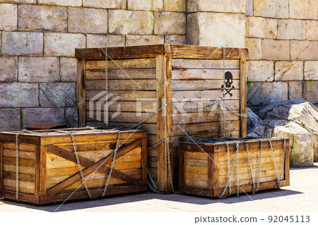 Wooden boxes with the image of a skull and crossbones wrapped in chains stand against the backdrop of a stone wall. Pirate treasure. Amusement park decor 92045113