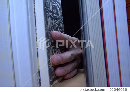 Behind the library, a human hand that picks up books, a bookshelf 92046016
