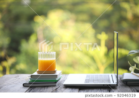 Laptop side view and mango juice in glass cup and notebooks 92046319
