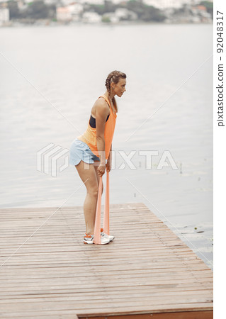 Sports girl by the water. Woman in a summer park. Lady in a orange sportswear. 92048317