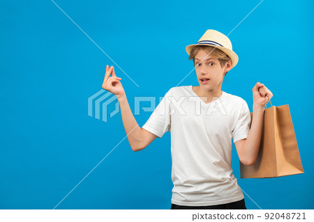 Surprised caucasian guy holding a shopping bags in his hand. Studio shot on blue wall. Surprised caucasian guy holding a shopping bags in his hand. Studio shot on blue wall. 92048721