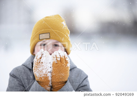 Child in winter. A little boy in a warm hat and mittens looks at the camera and smiles. 92049169