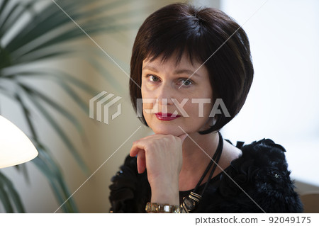 Portrait of a middle-aged woman forty or forty-five years old with an elegant haircut. An adult brunette woman looks at the camera. Portrait of a middle-aged woman forty or forty-five years old with an elegant haircut. An adult brunette woman looks at the camera. 92049175