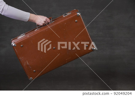 In hand is a brown retro suitcase on a gray background. 92049204