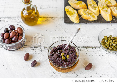 Olive pate in bowl and basic ingredients - olive oil, olives and capers on white wooden background 92050159