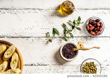 Olive pate with ingredients - olive oil, olives, capers on white wooden background with olive branch and crostini 92050160