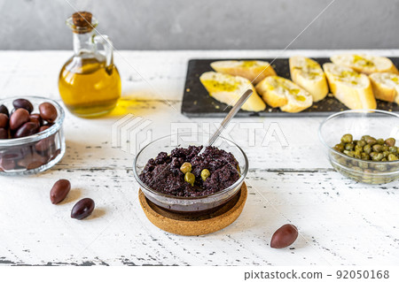 Olive pate in bowl and basic ingredients - olive oil, olives and capers on white wooden background Olive pate in bowl and basic ingredients - olive oil, olives and capers on white wooden background 92050168
