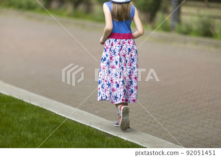 Little child girl in summer dress and a hat walking alone in green park. Little child girl in summer dress and a hat walking alone in green park. 92051451