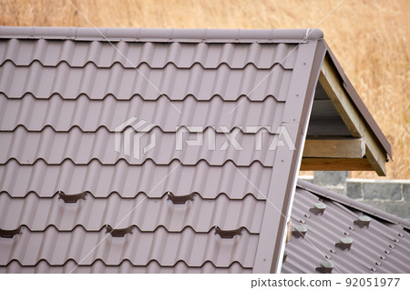 Closeup snow guard for safety in winter on house roof top covered with steel shingles. Tiled covering of building 92051977
