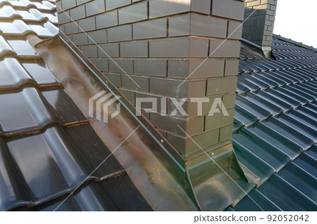 Closeup of brick chimney on house roof top covered with ceramic shingles. Tiled covering of building 92052042