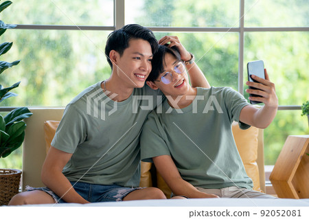 Couple gay or lgbt man enjoy with mobile phone together and sitting on sofa near bed in bedroom 92052081