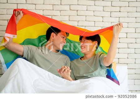 Couple Asian gay or lgbt man hold rainbow flag over their head and look at face of them 92052086