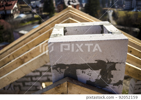 Close-up detail of roof frame of rough wooden lumber beams and chimney made of foam insulation blocks on blurred green background. Building, roofing, construction and renovation concept. 92052159