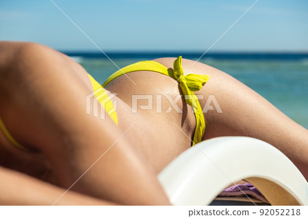Close up of young woman hip and shoulder laying on beach chair at sea shore sunbathing. Close up of young woman hip and shoulder laying on beach chair at sea shore sunbathing. 92052218