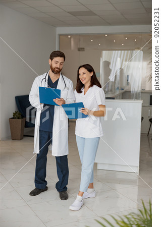 Two doctor colleagues discussing patient diagnosis stand in clinic hall 92052231