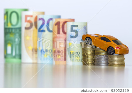 Blurred row of rolled hundred, fifty, twenty, ten and five new euro banknotes and pile of coins with yellow toy expensive sport car. Symbol of financial prosperity, vehicle sale and purchase. 92052339