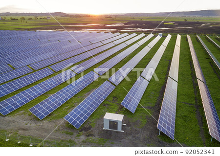 Blue solar photo voltaic panels system producing renewable clean energy on rural landscape and setting sun background. 92052341