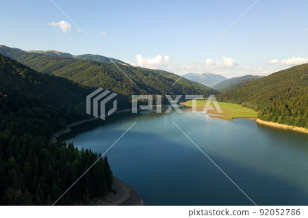 Aerial view of big lake with clear blue water between high mountain hills covered with dense evergreen forest. 92052786