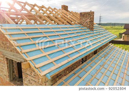 Aerial view of a brick house with wooden roof frame under construction. 92052804