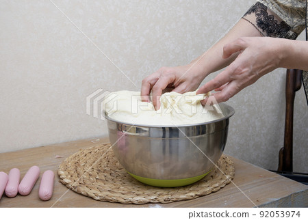Women's hands are kneading the dough in the home kitchen near the wall on the wooden table at the cozy farm house for making hot dogs and pies- close-up of women's hands. Mastery of cooking. 92053974