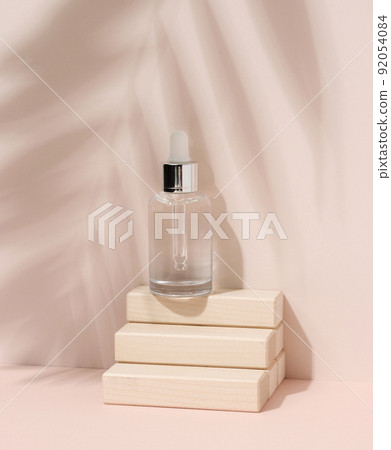 White glass bottle with a pipette on beige background. Palm leaf shadow White glass bottle with a pipette on beige background. Palm leaf shadow 92054084